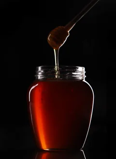 Amber-coloured honey in a jar with a wooden honey dipper; illustrative photograph.